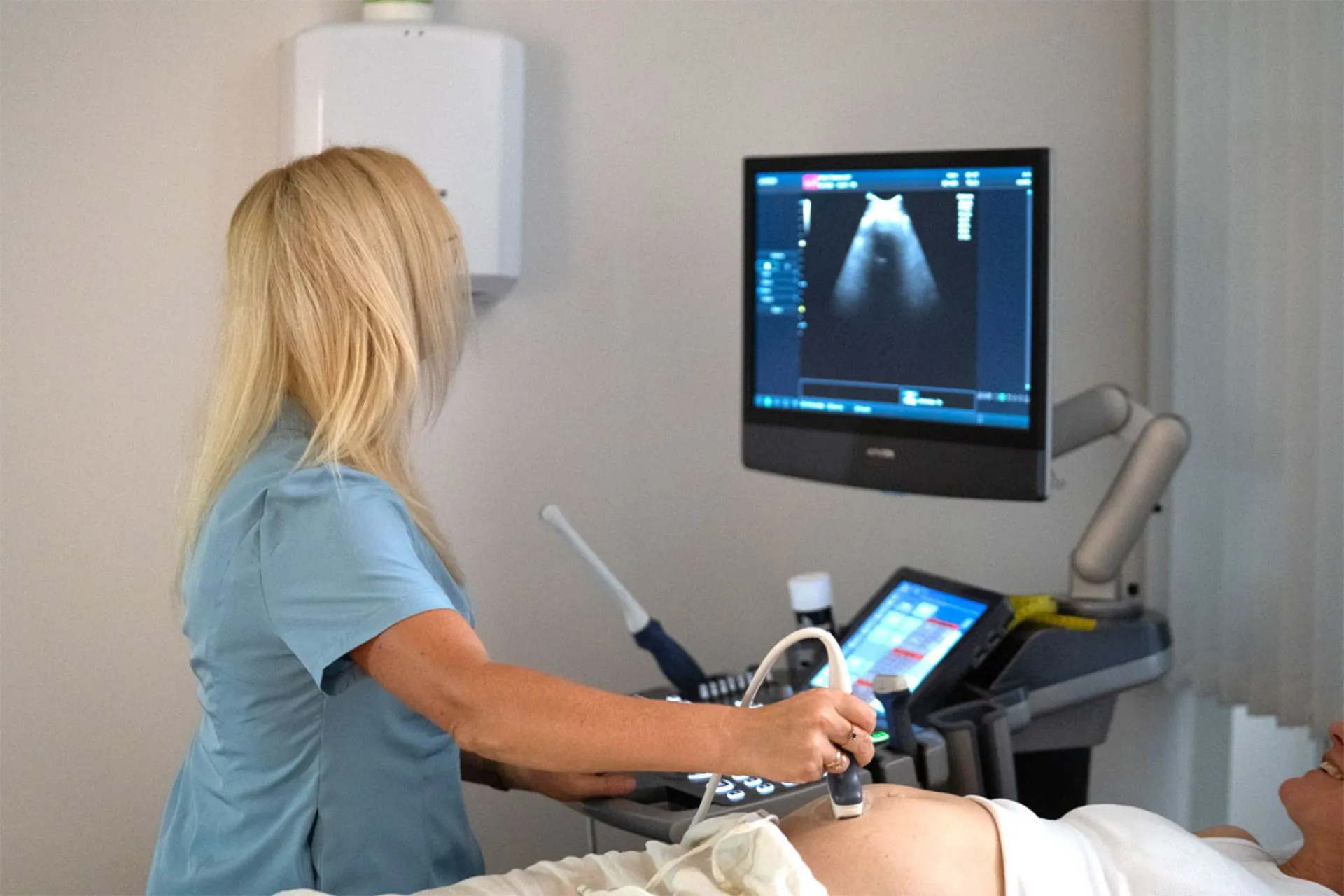 Dr. Aiga Rotberga ar USG aparātu izmeklē grūtnieci, kas guļ uz kušetes